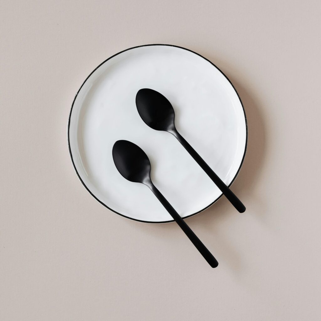 pexels-photo-4226876-4226876 Top view of black teaspoons placed on white ceramic plate with black border served on beige table